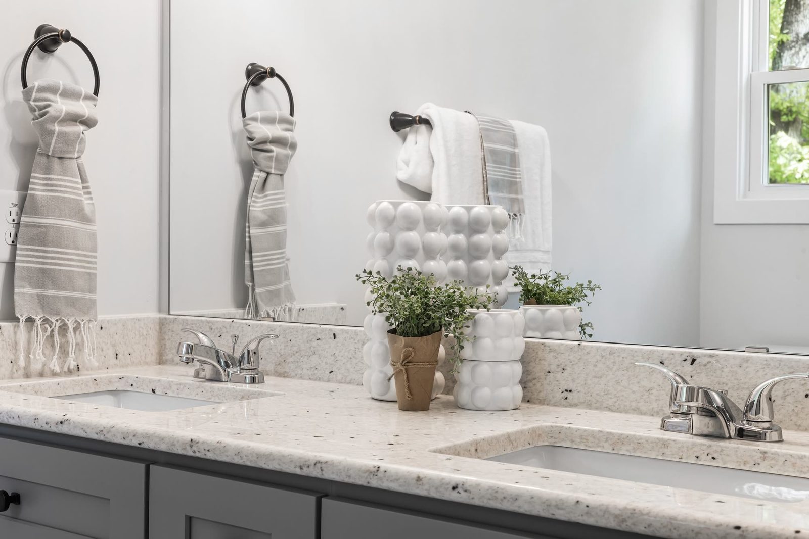 Bathroom vanity with grey stone countertop, mirrors, towel rings and decorative plants