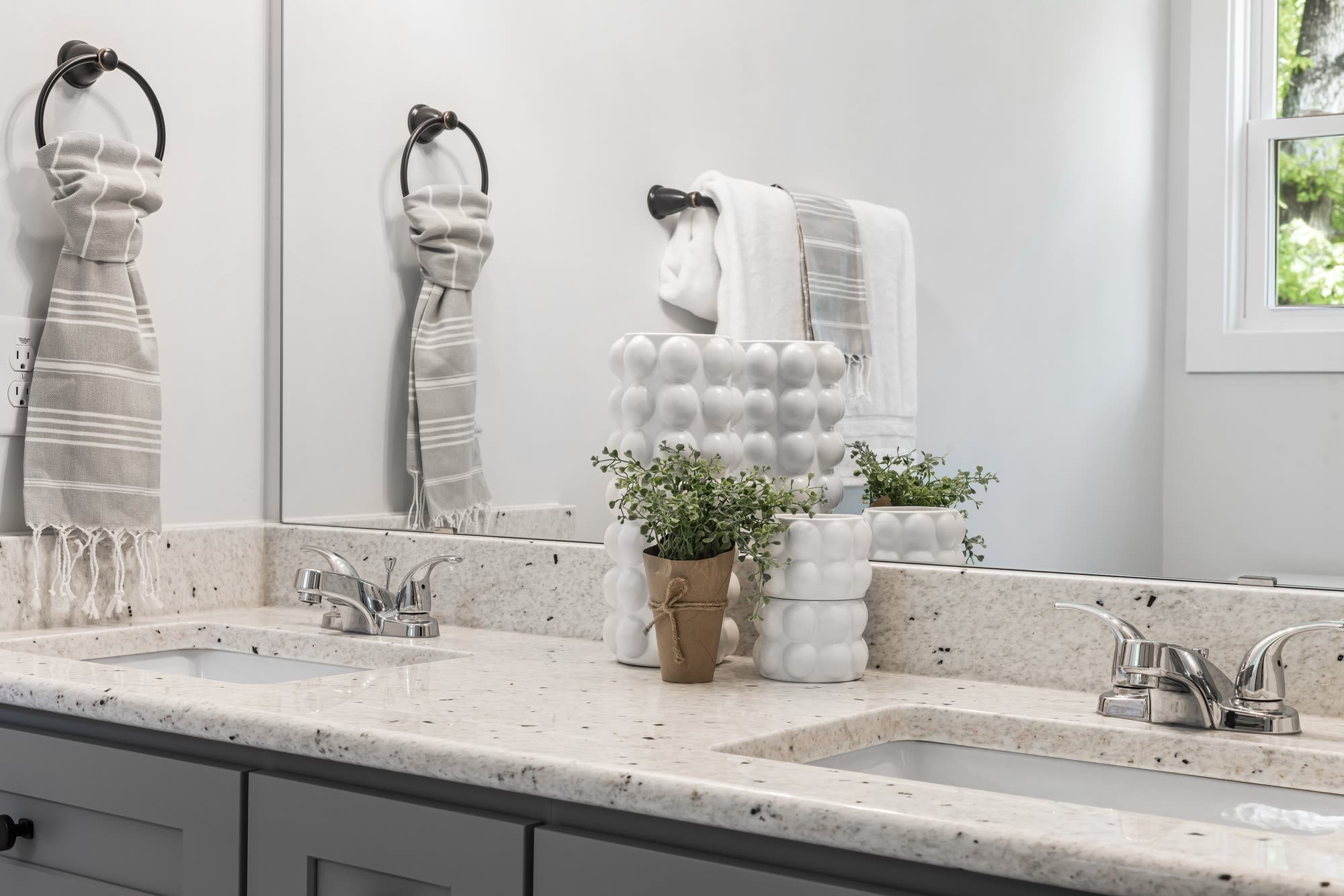 Bathroom vanity with grey stone countertop, mirrors, towel rings and decorative plants