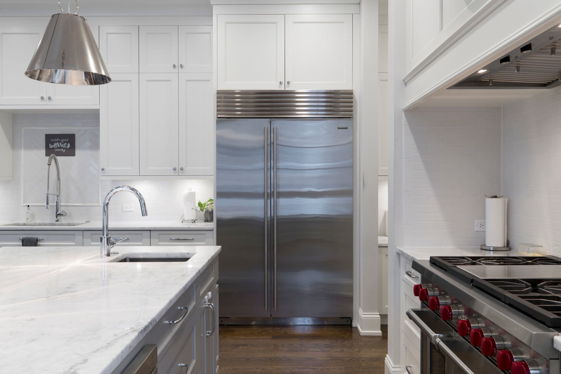Modern kitchen with white cabinets, stainless steel appliances and marble countertops, showing a professional renovation completed