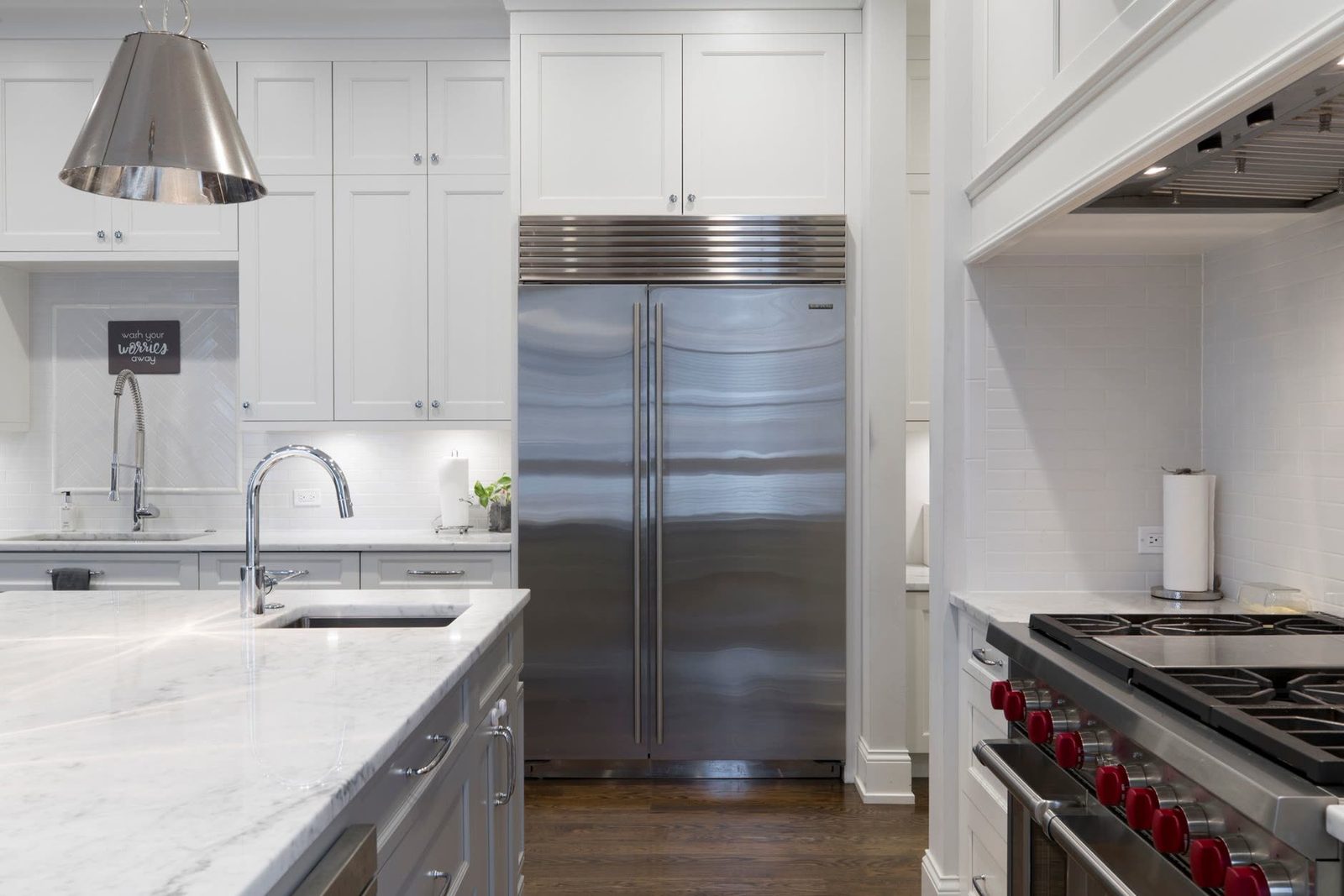 Modern kitchen with white cabinets, stainless steel appliances and marble countertops, showing a professional renovation completed