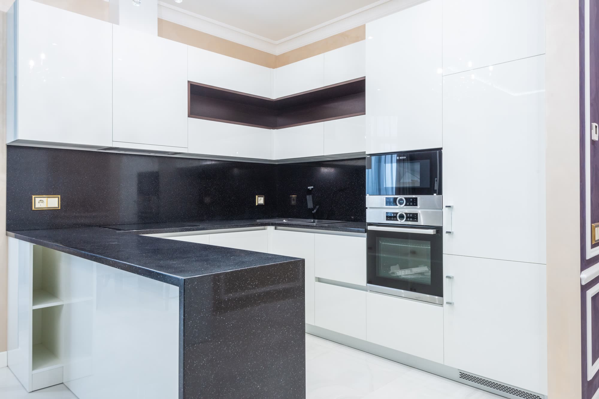 Modern kitchen interior with white cabinets, black countertop and stainless steel appliances, professionally installed contemporary design, bright kitchen space with natural lighting